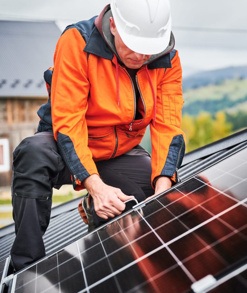 Man technician mounting photovoltaic solar panels on roof of house with help of hex key. Man builder mounting photovoltaic solar panels on roof of house. Engineer in helmet installing solar module system with help of hex key. Concept of alternative, renewable energy.
